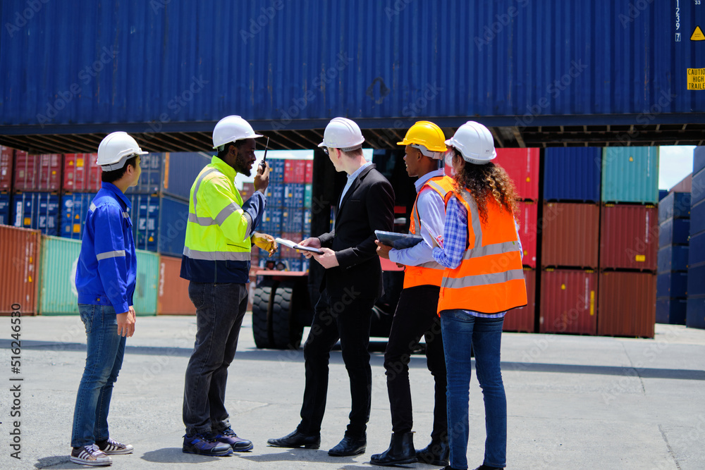 Group of multiracial workers in safety uniforms and hardhats work at logistics terminal dock with stacks of containers, loading control, and management shipping goods, cargo transportation industry.