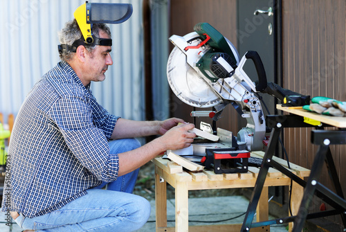 a handyman in a protective helmet works with a miter saw photo