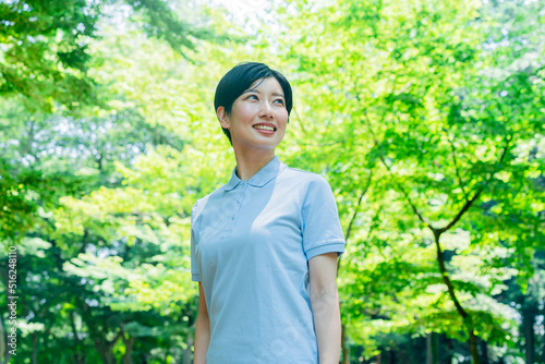 新緑の中、笑顔で笑うポロシャツを着た日本人女性