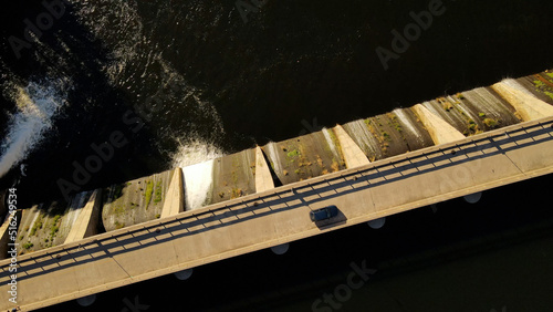 Aerial top down shot of vehicle driving on dam road crossing lake during sunny day in Argentina