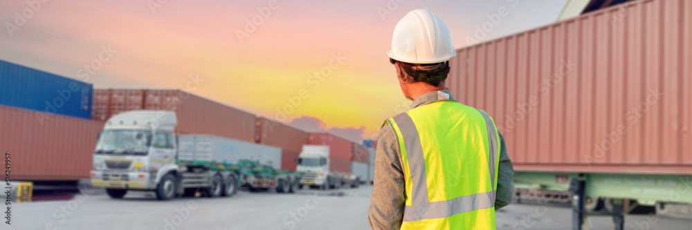 A truck driver wearing a helmet stands in a parking lot. A truck driver wearing a helmet stands in a parking lot.