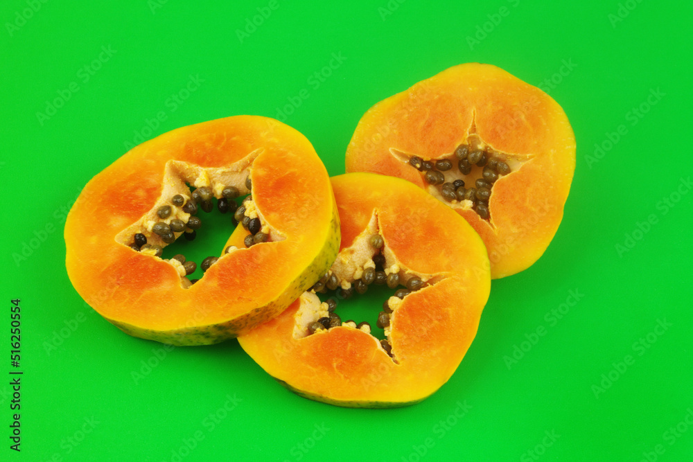 Slices of papaya fruits on green background close-up.