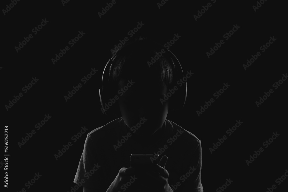 profile of a child in headphones looking at a phone in complete darkness
