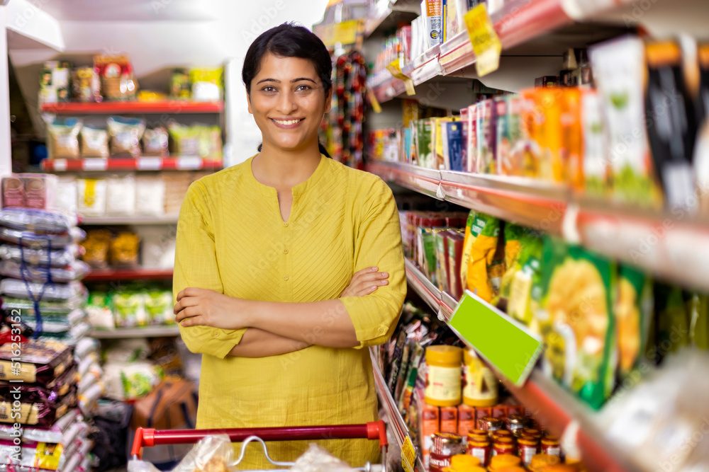 Happy woman owner with arms crossed at grocery aisle of supermarket