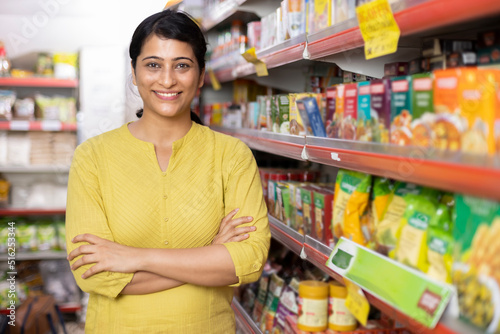 Happy woman owner with arms crossed at grocery aisle of supermarket