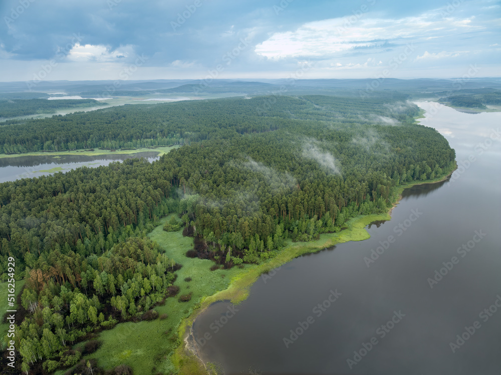 Big lake with green shores with morning fog in dawn, aerial landscape. Recreation concept. Aerial view