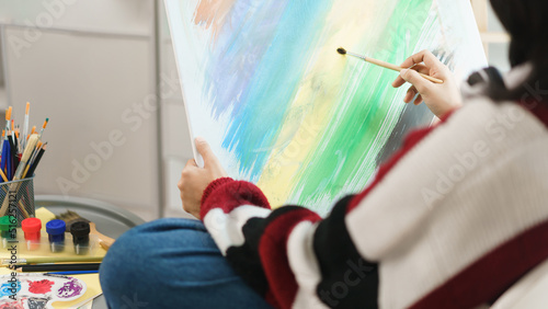 The art concept, Asian female artist sitting on the chair and holding canvas to painting artwork