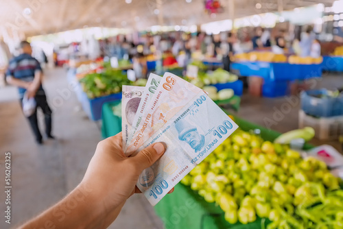 Turkish lira banknotes in hand against the background of vegetables at the farmer's market. The concept of consumer economy and inflation of the national currency of Turkey. photo