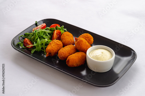 Quadro su tela A plate of fried breaded surimi crab claws with a bowl of white sauce, sliced ​​tomato and arugula