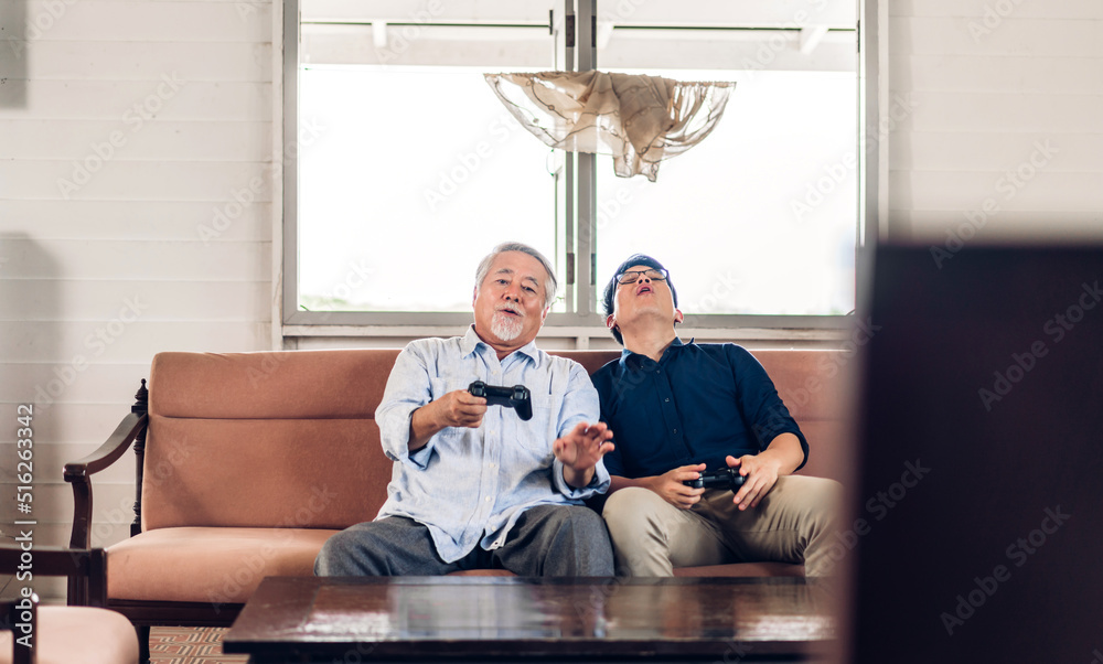 Portrait of happy love asian family senior mature father and young man adult son having fun enjoy holding gamepad controller play console video game together at home