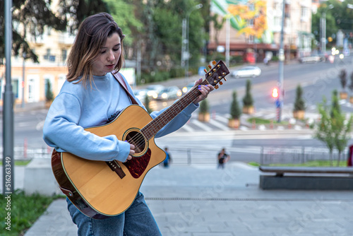 Female musician busking playing acoustic guitar and singing outdoors in street. photo