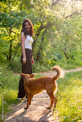 Young beautiful smiling woman walking with her dog in the park