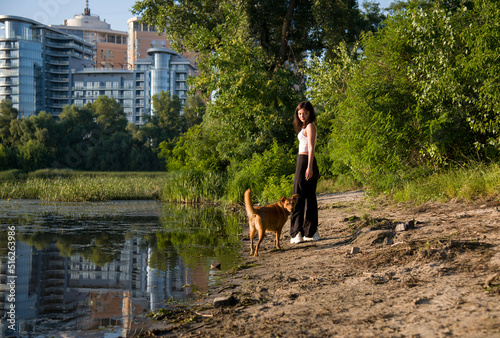 Young beautiful smiling woman walking with her dog at the river