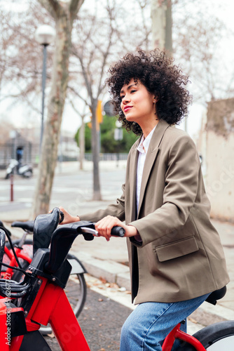 young latin woman rides an electric bike from a rental station, active lifestyle and sustainable mobility concept