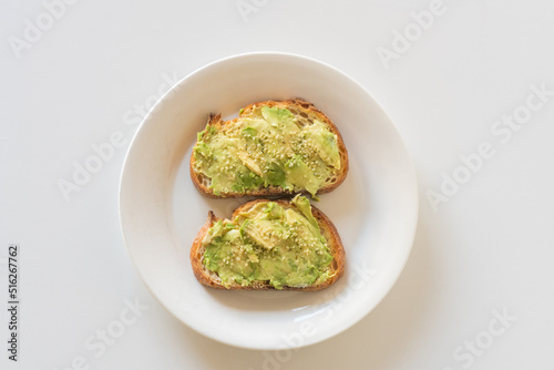 High angle closeup of toasted sourdough bread with avocado and hemp seeds on white plate