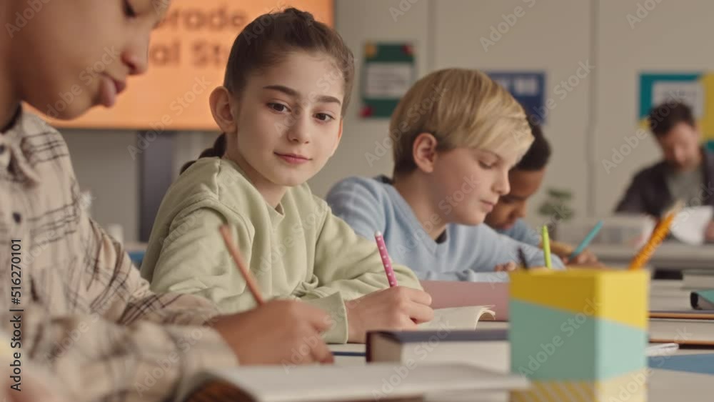 Chest up slowmo of pretty school girl looking at classmate copybook while taking test in classroom Chest up slowmo of pretty school girl looking at classmate copybook while taking test in classroom