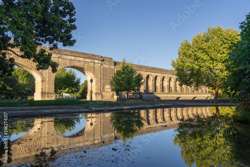 Scenic summer morning landscape view of St Clement aka Arceaux aqueduct ancient stone building with reflection in pool in historic Promenade du Peyrou garden, famous landmark of Montpellier, France