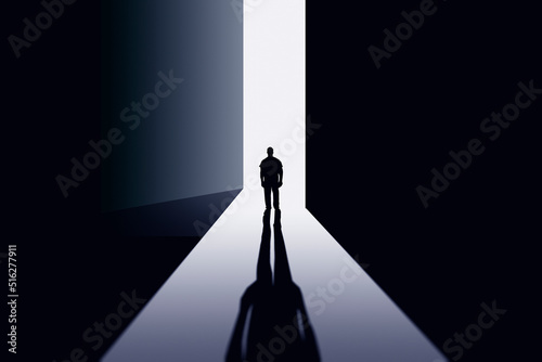A man stands in the doorway of a large ajar door in the rays of light.
