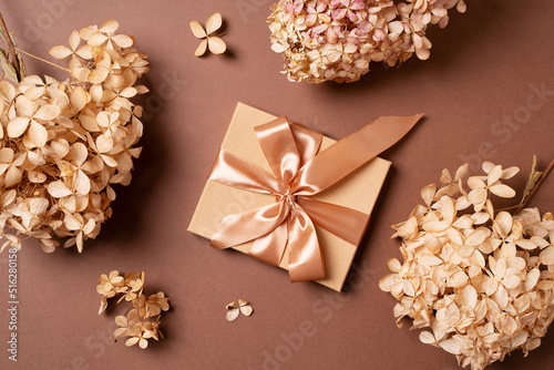 Gift box with golden ribbon and dry grass and flowers on brown background