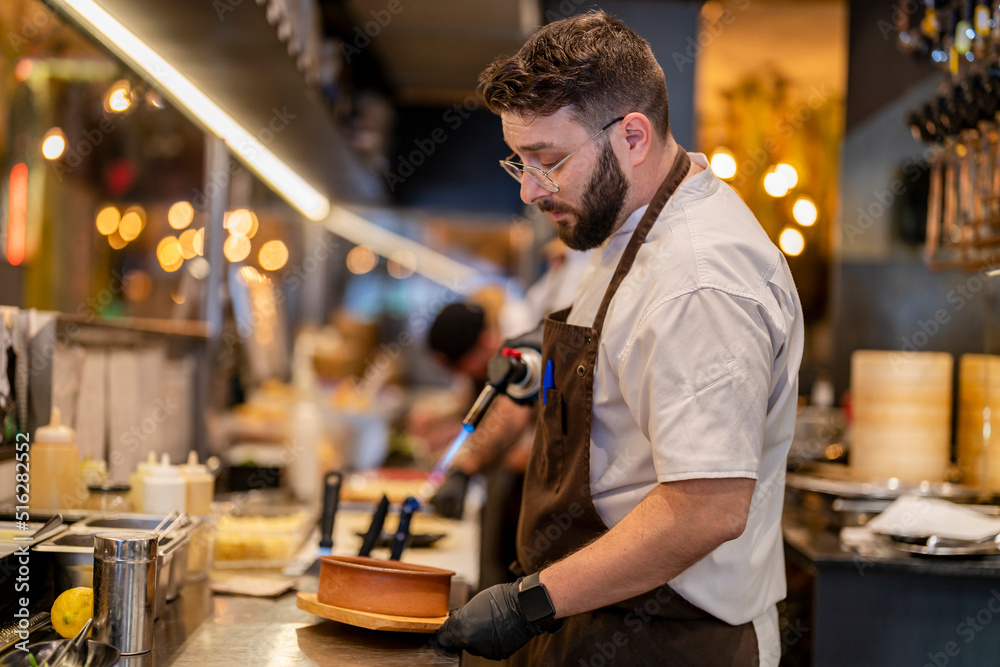 Chef using flaming torch standing at restaurant kitchen Chef using flaming torch standing at restaurant kitchen