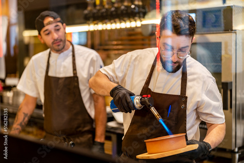Chef using flaming torch standing with colleague at restaurant photo