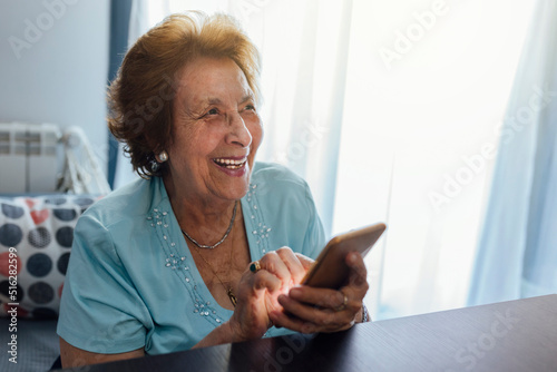 Happy senior woman with smart phone sitting at home photo