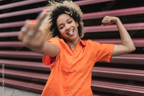 Carefree woman flexing muscles making obscene gesture in front of wall