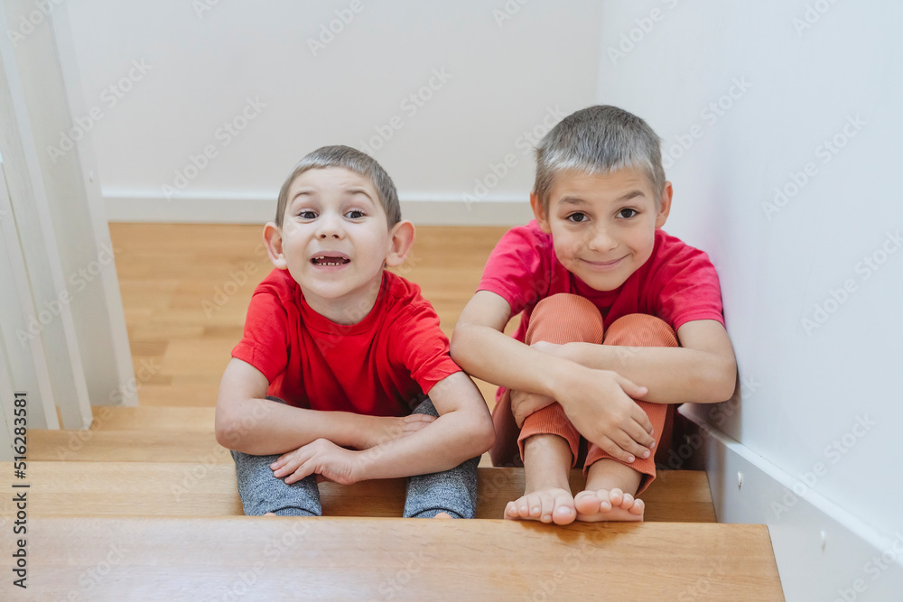 Brothers hugging knees sitting on staircase at home Brothers hugging knees sitting on staircase at home