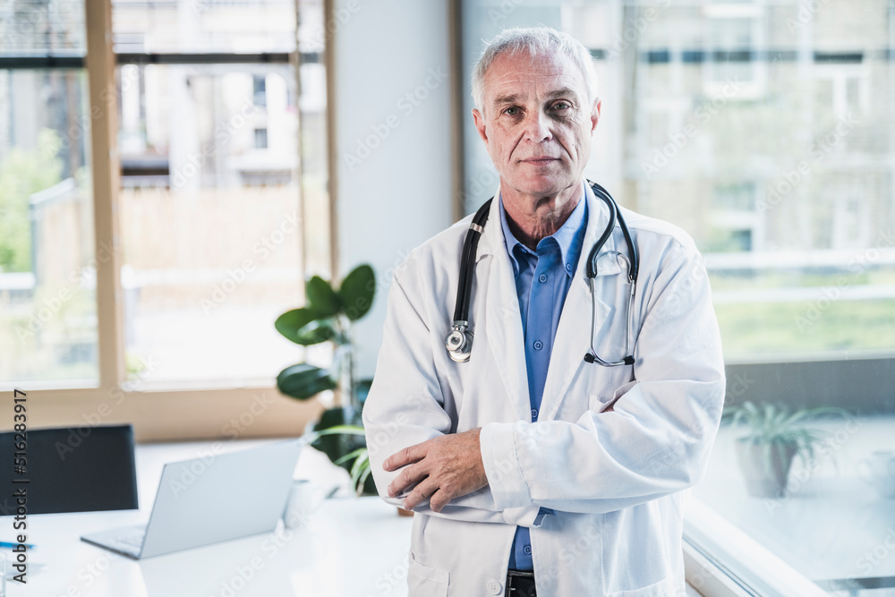 Senior doctor with arms crossed standing in office