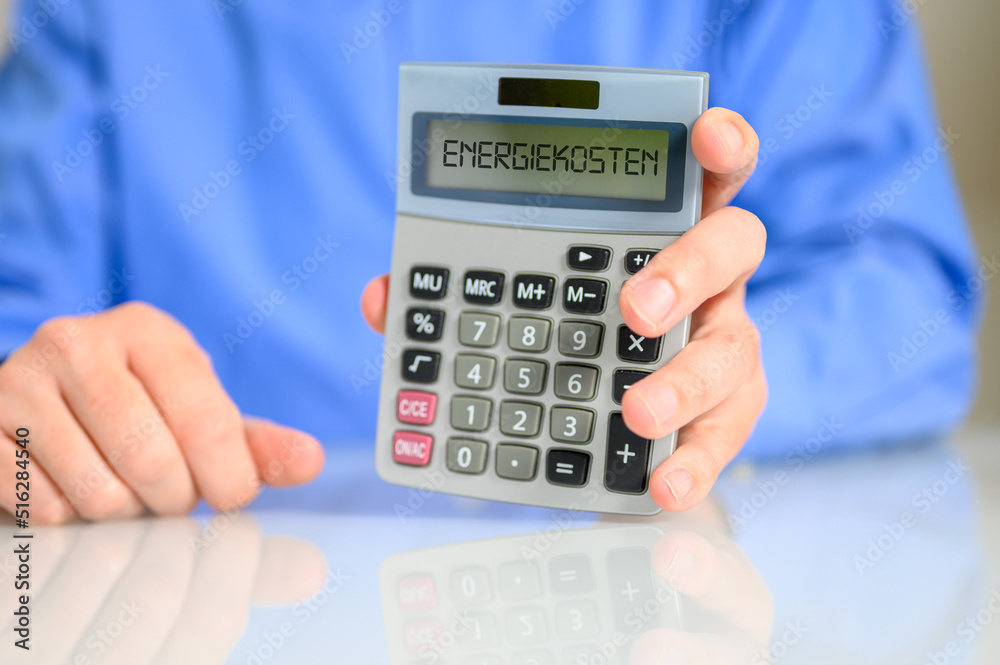 Mann am Schreibtisch mit einem Taschenrechner auf dem ENERGIEKOSTEN steht Mann am Schreibtisch mit einem Taschenrechner auf dem ENERGIEKOSTEN steht