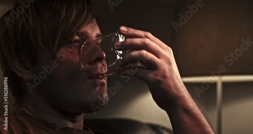 A man drinks a glass of alcohol in a dark room