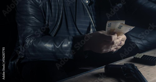 a mobster or drug dealer is counting money and has a gun on the table photo