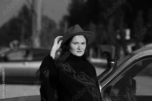 Young woman in a hat standing near the car in black and white