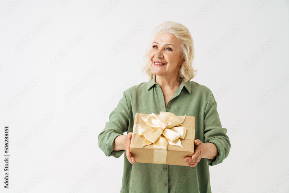 Grey senior woman smiling while showing gift box at camera Grey senior woman smiling while showing gift box at camera