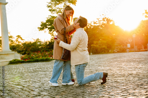 White man proposing to his excited girlfriend in park