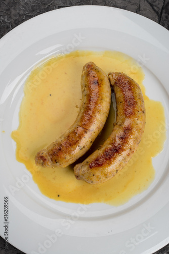 two large fried bavarian sausages with sauce in a white plate
