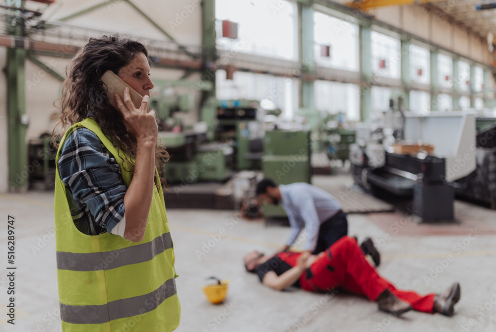 Woman is calling ambulance for her colleague after accident in factory. First aid support on workplace concept. - obrazy, fototapety, plakaty 
