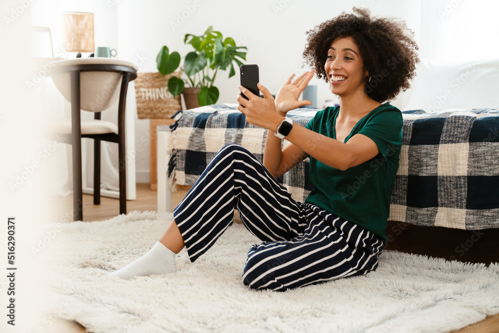 African american young woman smiling and using cellphone at home African american young woman smiling and using cellphone at home