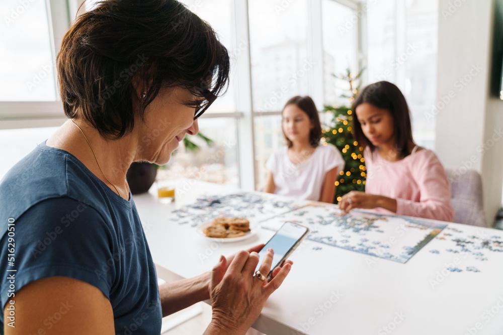 Multiracial sisters doing puzzle while their mother using cellphone Multiracial sisters doing puzzle while their mother using cellphone
