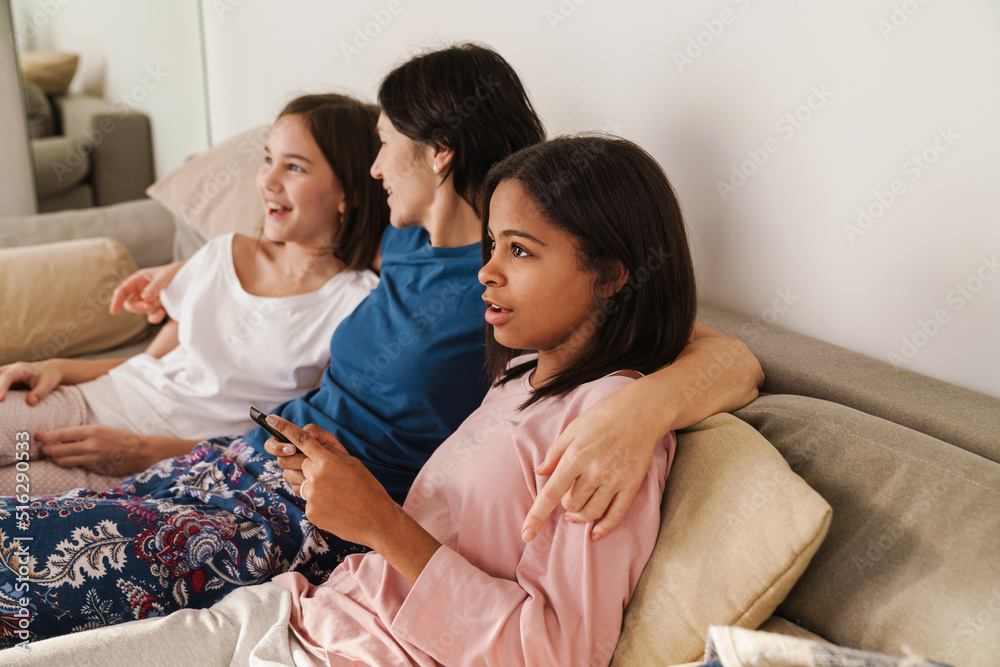 White woman and her daughters watching tv while resting on couch White woman and her daughters watching tv while resting on couch