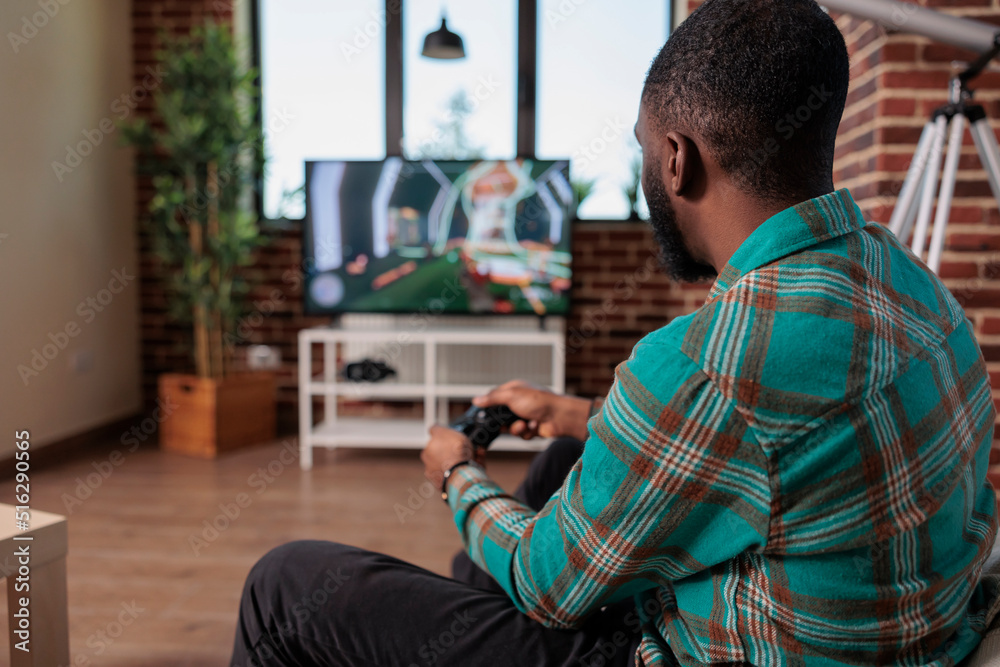 African american man using controller and console to play shooting game, enjoying leisure activity with video games competition. Young adult having fun with shooter gaming strategy.