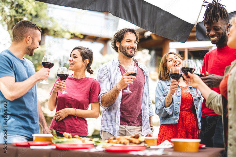 Group of happy friends having fun while drinking red wine and eating food at party, focus on young bearded handsome man, genuine people