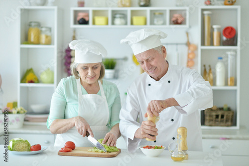 Portrait of couple of smiling senior chefs at kitchen