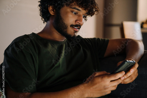 Young handsome indian man using his phone sitting on sofa photo