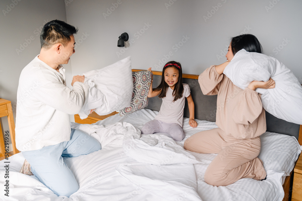 Asian family with little girl fighting with pillows together in bed