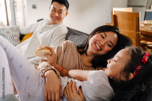Happy asian family with little girl laughing while sitting on sofa