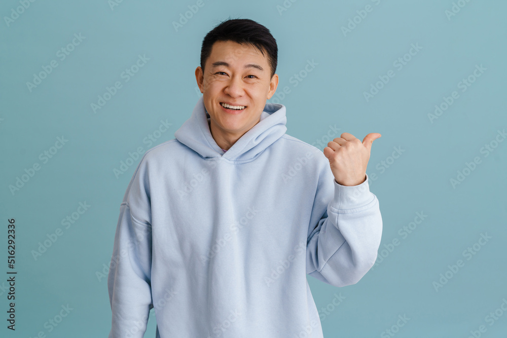 Brunette adult asian man smiling and pointing aside at copyspace Brunette adult asian man smiling and pointing aside at copyspace