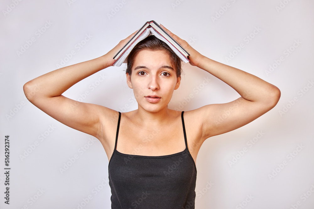 The girl holds open books on her head. The concept of hard training. The girl holds open books on her head. The concept of hard training.
