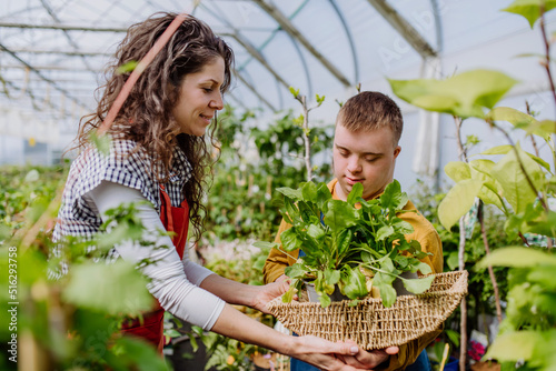 Experienced woman florist helping young employee with Down syndrome in garden centre. photo