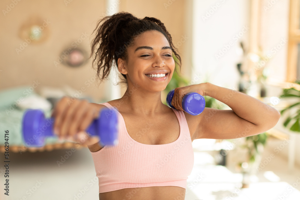 Training with weights. Happy african american woman doing exercises with dumbbells, strengthening her body at home